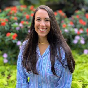 Julia Spielmann wearing a blue collared shirt and standing in front of bushes with red flowers