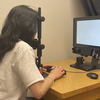 A student sitting at the desk in from of the monitor and an eye tracking camera holding a button box in her hands